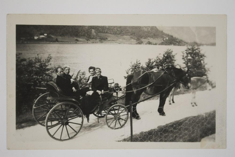 Då vegen var ferdig frå Holmen (Balestrand sentrum) til Ese i 1895, var det stor fest. Bygdepoet, kyrkjesongar og klokkar A. P. Øvrebø dikta ei vise til festen, der eitt av versa går slik: 

"Og skranglekjerrer og skjeive meier/ 
Og fillegampar og vidjegreier/
Det kverv nok burt etter denne dag./ 
Jau, eg skal sei her vert anna slag."

Og som vi ser er i alle fall køyredoningen ganske fine. Hest og karjol er på veg til Holmen. Damene bak i vogna er Marie Tuftedal og Brita Sundal. Framme sit T...